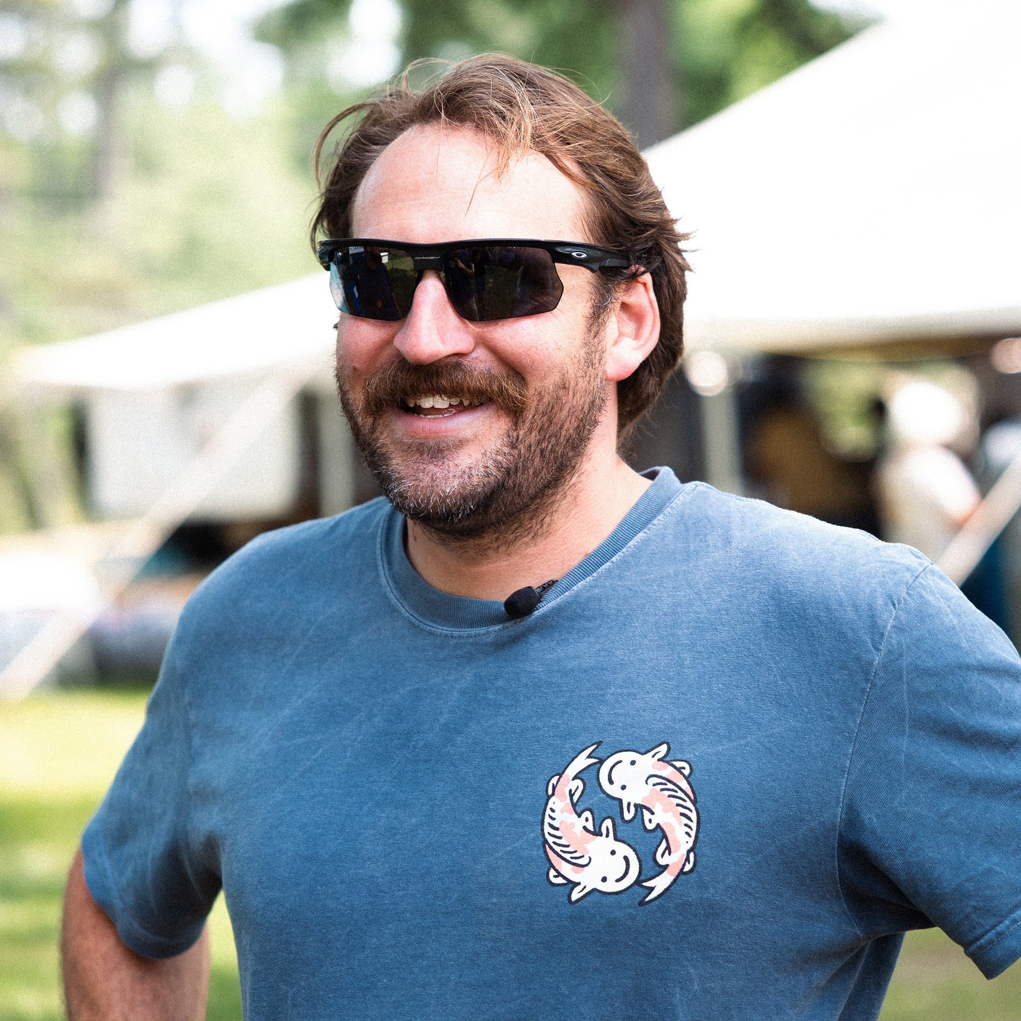 Cooper wearing sunglasses and a blue t-shirt with a white design outdoors