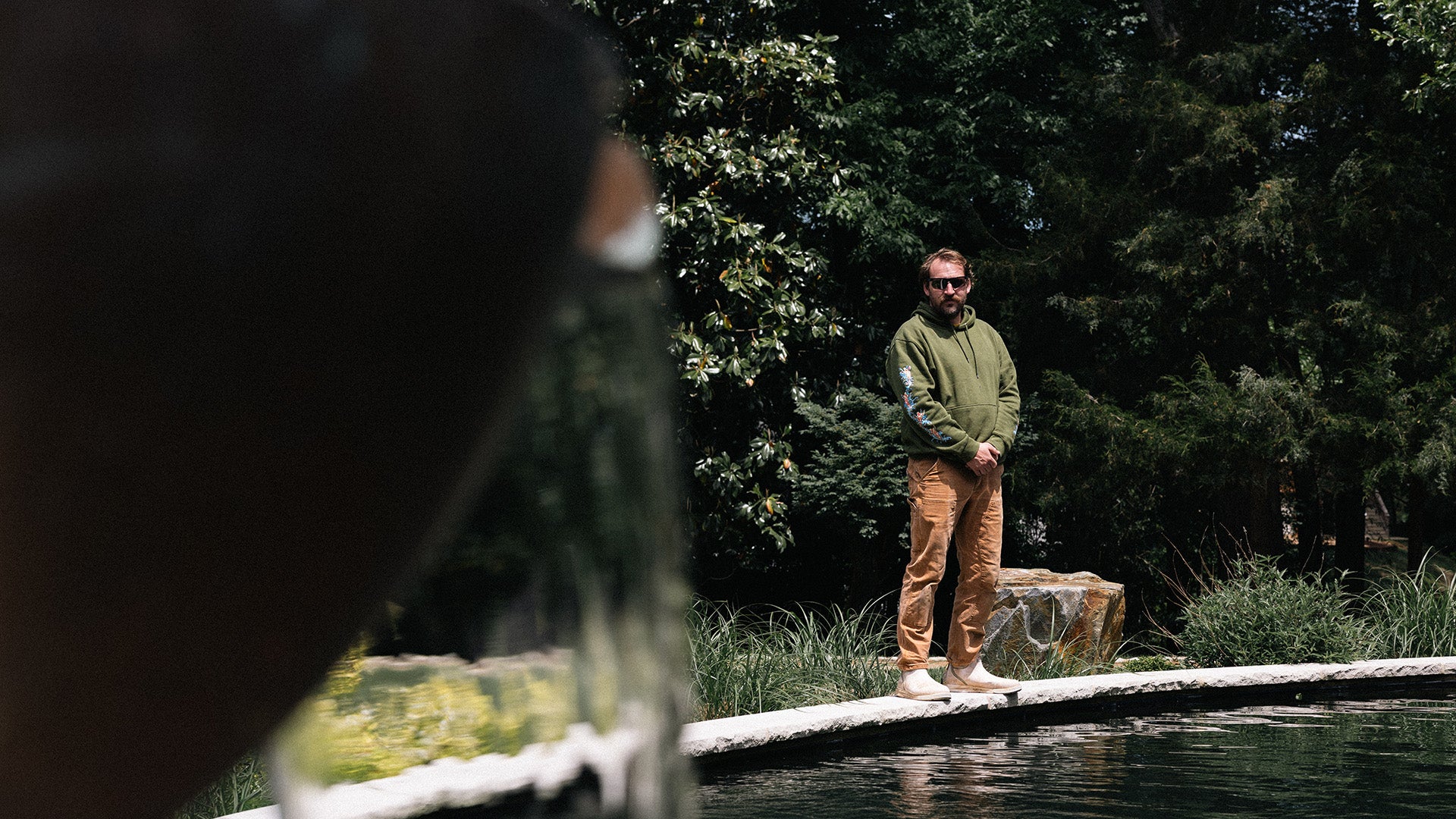 Aqua Fauna owner Cooper standing on a rock by a body of water with trees in the background